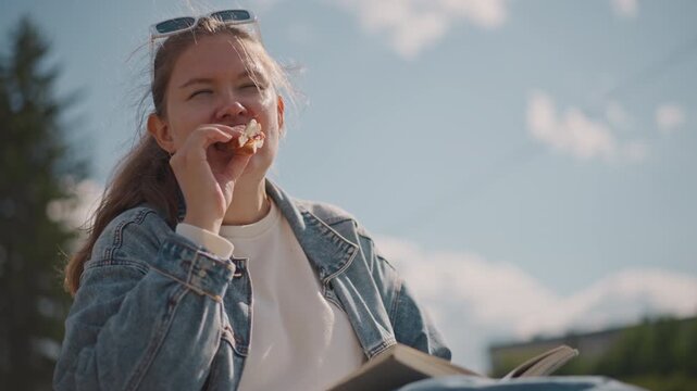 Outdoor reading happiness. Woman enjoys book beneath sun. Relaxing woman in denim treasures outdoor book experience. Woman in casual attire finds pleasure reading outside under bright sunlight