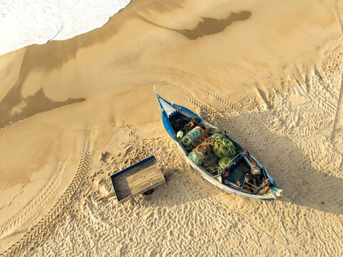 Aerial view of a traditional blue fishing boat filled with nets and gear on the sandy beach of Praia de Mira with tire tracks and ocean waves Praia de Mira, Coimbra, Portugal.
