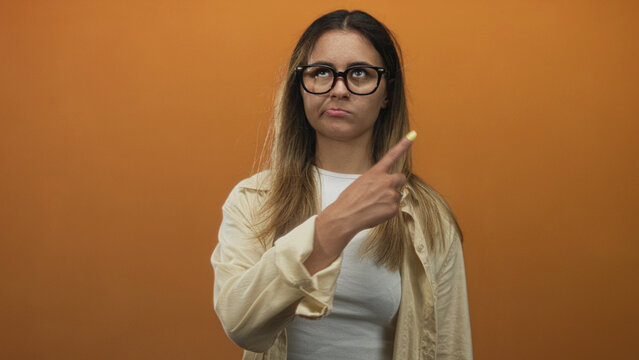 Woman crossing arms and pointing fingers showing yellow nails in studio with orange backdrop; defiance.