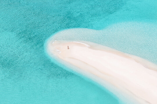 Aerial view of a person standing on a pristine white sandbank surrounded by crystal clear turquoise waters in Dhidhdhoo, Haa Alif Atoll, Maldives.