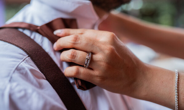 Primer plano de anillo de compromiso mientras una mujer ajusta la corbata de su pareja antes de la boda