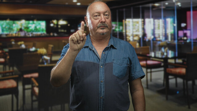Man points finger at camera in a restaurant building, raising index finger in a clear pointing gesture; assertive warning.