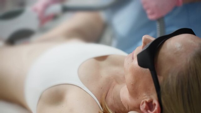 Woman undergoing professional laser hair removal treatment in aesthetic clinic, wearing protective glasses during modern cosmetic skincare procedure for smooth skin.