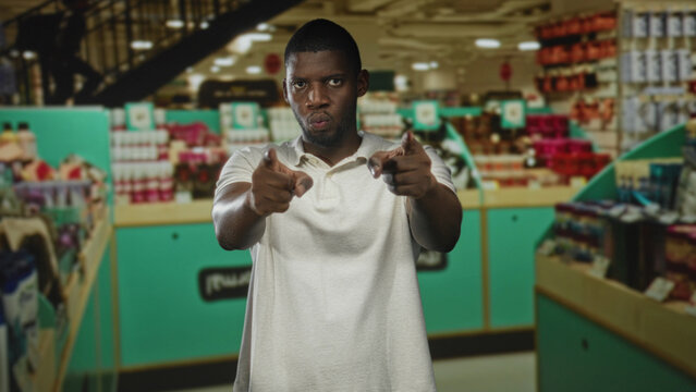 Man points finger at camera with visible fingers and white polo in retail building; assertive challenge.