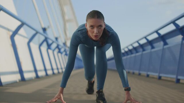 Determined young sportswoman in starting position preparing for outdoor running session, 4K