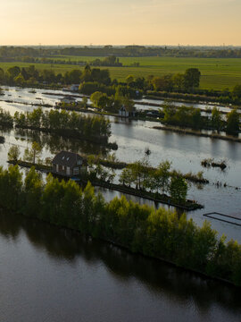 Breukelen, Netherlands - 25 April 2026: Aerial view of Scheendijk recreational area featuring narrow strips of land with houses and lush trees surrounded by calm water during golden hour.