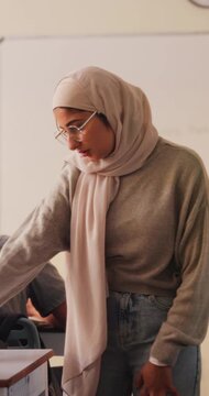 Woman, teacher and talk with students in classroom for exam, assistance and education. Muslim, educator and helping children with test instructions, academic assessment and learning support at school