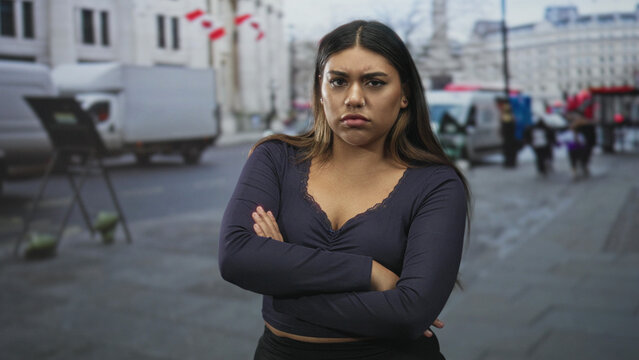 Woman with arms crossed and stern expression on a city street in navy vneck longsleeve shirt; frustration defiance.