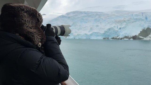Female Photographer on Antarctica Cruise Ship Close Up Over the Shoulder. Wearing Fur Hat and Black Jacket with Telephoto Lens. Glacier Ice and Snow