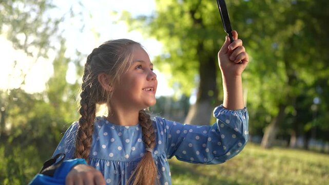 the girl holds a magnifying glass in her hands. gaining knowledge and curiosity concept. lifestyle a schoolgirl girl with a black magnifying glass is examining something, park on the background