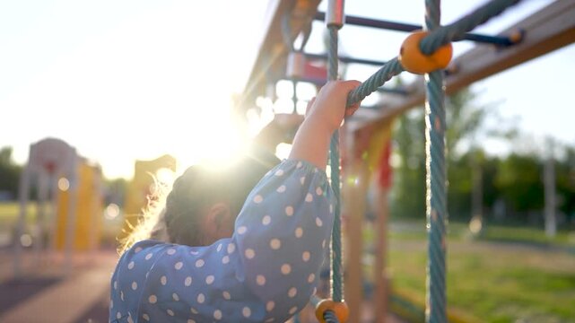 child plays on the playground. concept of a happy childhood and loving family. a child smiles joyfully and climbs a ladder on a playground, the glare of the sun lifestyle in the background