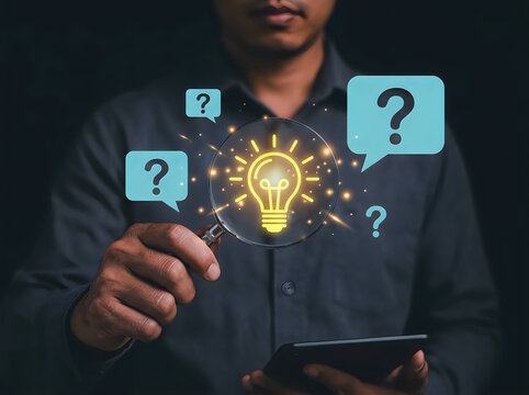 Person holding a magnifying glass over a glowing light bulb surrounded by question marks symbolizing creativity and problemsolving