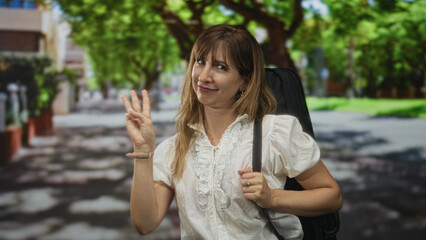 Fototapeta premium Woman holding three fingers up with instrument case on shoulder, wearing white blouse and wristwatch in street; playful casual travel.