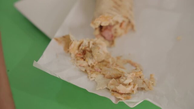 Messy wrap on green table, closeup hand picking torn pita on paper intimate candid moment during casual date, shy laughter, crumbs and sauce textures, soft warm light, relatable food fail