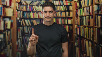 Man in black t shirt pointing index finger at bookshelves in a public building, mild frown and raised finger gesture  study focus thoughtful. © Krakenimages.com
