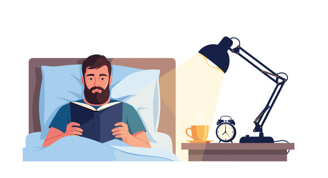Man sitting up in bed and reading a book by the light of a desk lamp with a cup of tea and an alarm clock on the bedside table at night.