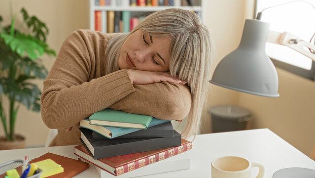 Woman resting head on a stack of books at a desk beside a lamp in a building, leaning on forearms after studying; fatigue study burnout.