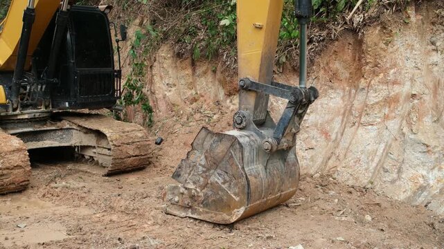Yellow excavator digging through muddy construction site with large bucket and piles of dirt. Industrial machinery working on earthmoving project outdoors.