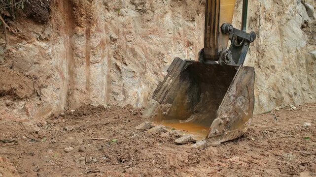 Close up of excavator bucket filled with wet soil and mud at construction site with copy space on left side. Industrial earthmoving machinery detail.