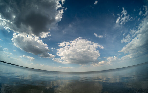 Wide-angle fisheye view of a large calm lake reflecting white summer cumulus clouds in calm water
