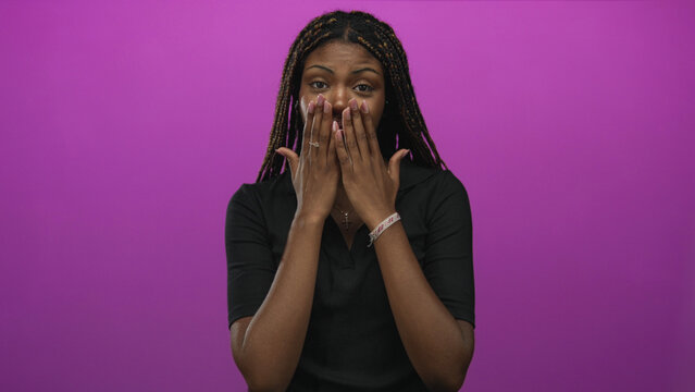 African american woman with hands over mouth and hand on chest, braided hair and cross necklace in purple studio; apologetic regret.