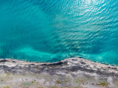 Seaside aerial snapshot. Drone captures coastline with water movement. Underside view from drone illustrating architecture of water and wave patterns at coastline