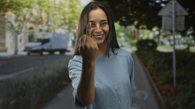 Young hispanic woman shows middle finger on city street in daylight, standing near bike lane and parked van; defiance.