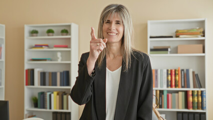 Woman clapping hands and smiling, middleaged blonde in black blazer before bookshelves in office building  warm encouragement. © Krakenimages.com