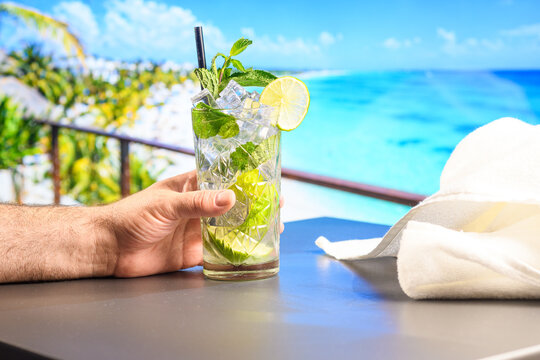 Hand holding fresh mojito by turquoise tropical sea