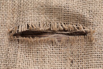 Obraz premium Burlap fabric with torn hole on wooden table, top view