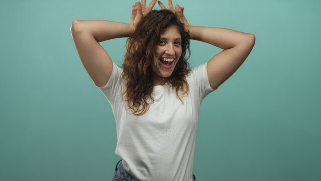 Woman wearing white t shirt with hands making bunny ears, bare arms visible, smiling in a mint studio; joy spontaneity energy.