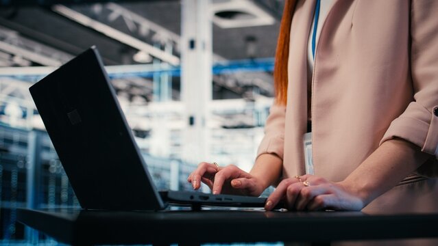 Close up of engineer typing on laptop in server farm, doing network management virtualization, Data center admin overseeing large scale IT infrastructure supercomputers with notebook, camera A.