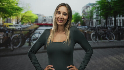 Fototapeta premium Woman with hands on hips showing shoulders at street canal in amsterdam; confidence travel exploration.