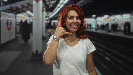 Fototapeta premium Woman showing call hand gesture and smiling in a building platform with visible watch and pillar in frame; playful joy.