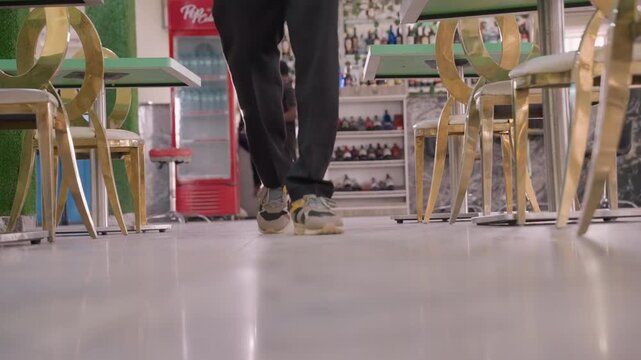 Shoes approach romantic cafe. Young man walks to table anxiously. Sneakers scuff floor as man approaches table. Gentle lighting sets mood while nervous steps near romantic meeting spot