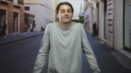 Obraz premium Man shrugging shoulders with closed eyes in a grey sweater on a cobblestone street, slight smirk and relaxed stance; uncertainty.