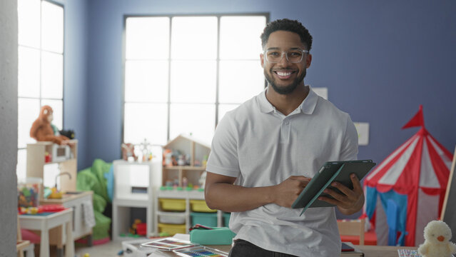 Man with tablet tapping screen, smiling, hands visible in a preschool building; friendly teaching care.