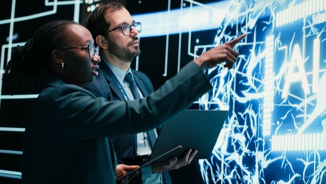 Engineering team coworkers receive tasks from autonomous agentic AI, working together, Teamworking colleagues talking with artificial intelligence superintelligence projected on digital wall.