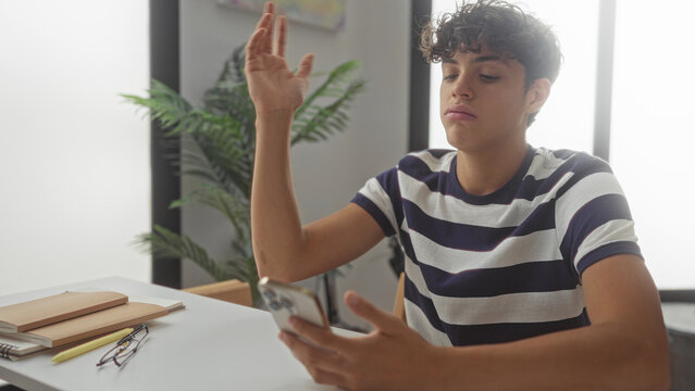 Man holding smartphone and tapping screen at a desk with notebooks and glasses in a building; boredom distraction.