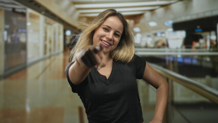 Fototapeta premium Woman pointing finger at camera showing hand and smile in mall building center; youthful confidence.