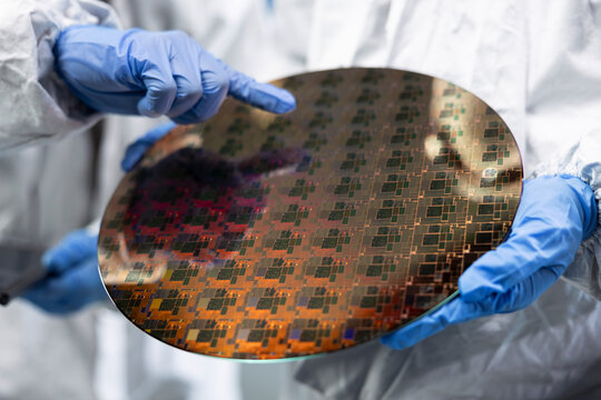 Working together, silicon wafer close up and men in automated fabrication plant cleanroom, Examining semiconductor substrate, bunny suit and coworkers analyzing microelectronics defects.