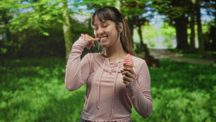 Fototapeta premium Woman holding ice cream cone, pointing finger and smiling on a forest path while eating and gesturing; joyful play.