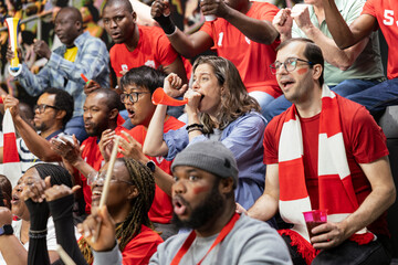 Red team football supporter blowing red vuvuzela and cheering in stadium stands during intense soccer match. Sports fans keeping rhythm for team support and football culture. © DC Studio