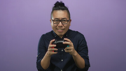 Young man holding a game controller with hands and tense expression in studio against purple wall  frustration competition. © Krakenimages.com
