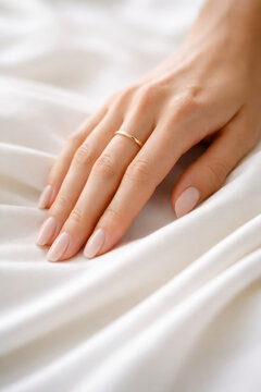 Elegant hand with nude nails and gold ring on satin fabric
