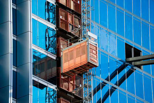 Construction elevator attached to a modern glass skyscraper under bright blue sky