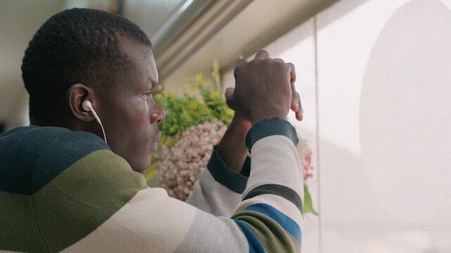 Gentleman happily gazes at indoor floral arrangements. Seated man by window admires lovely indoor flower decorations. Man sitting by window sincerely appreciates stunning display of indoor blossoms
