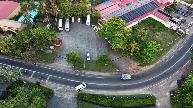 Aerial view of vehicles driving on a curved road next to a parking lot with buses and buildings with solar panels in Galle, Southern Province, Sri Lanka.