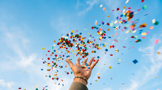 Hand throwing colorful confetti into blue sky celebrating academic success