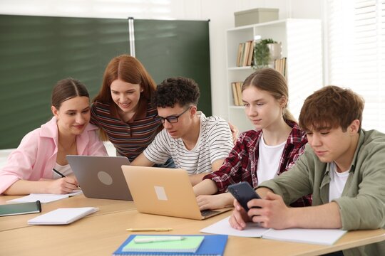 Group of students studying with laptops and notebooks at wooden desk in classroom